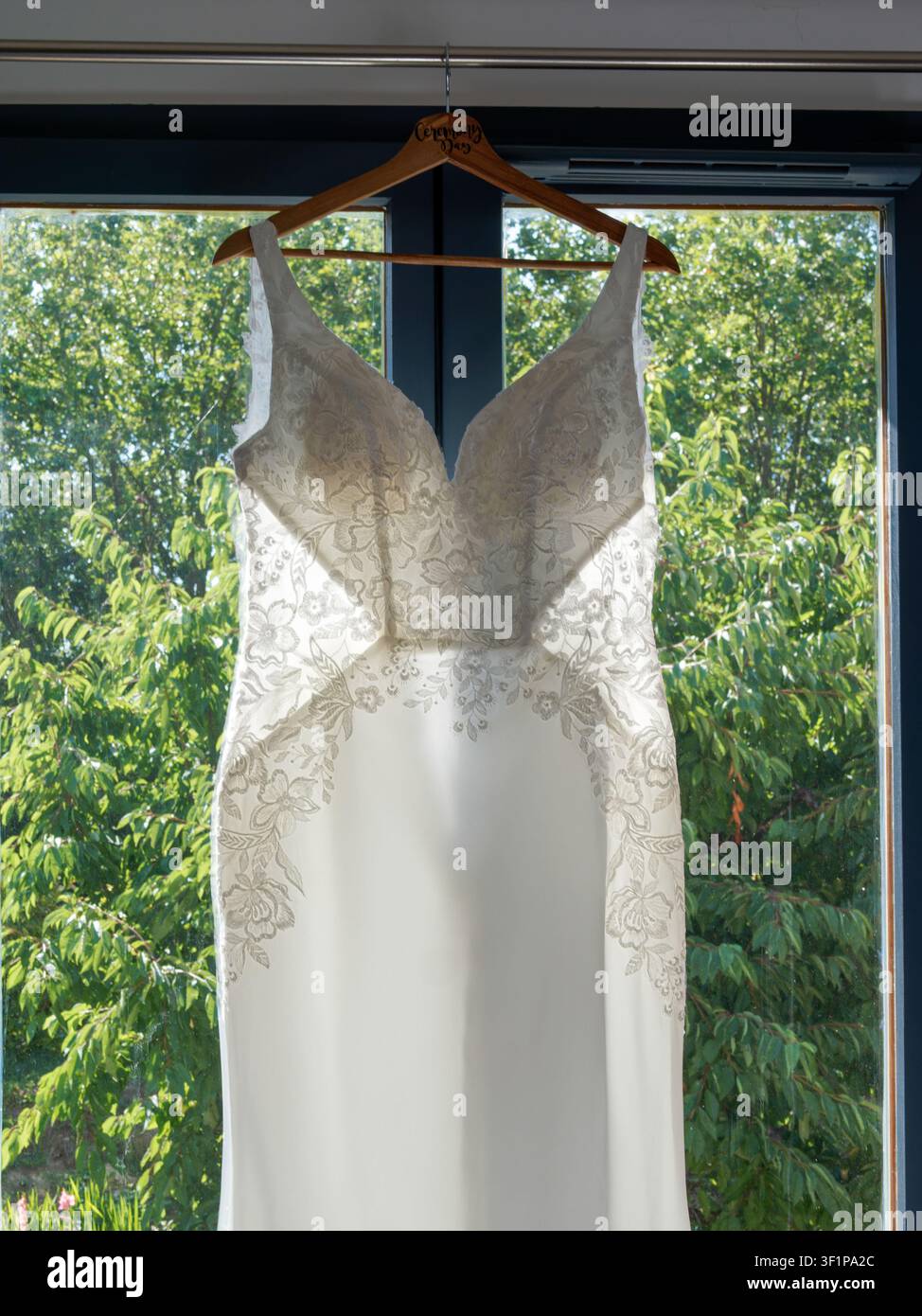 Robe de mariée élégante en dentelle blanche suspendue devant une fenêtre avant la cérémonie Banque D'Images