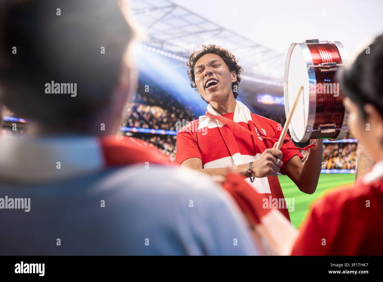 Homme passionné dans un stade de football battant un tambour pour rallier les supporters. Chef de fans énergisant un large public dans les tribunes d'une salle sportive lors du jour du match Banque D'Images
