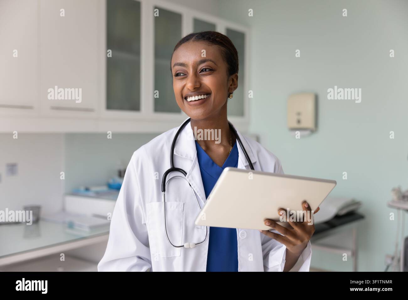 Jeune médecin noire joyeuse tenant une tablette dans un bureau de clinique Banque D'Images