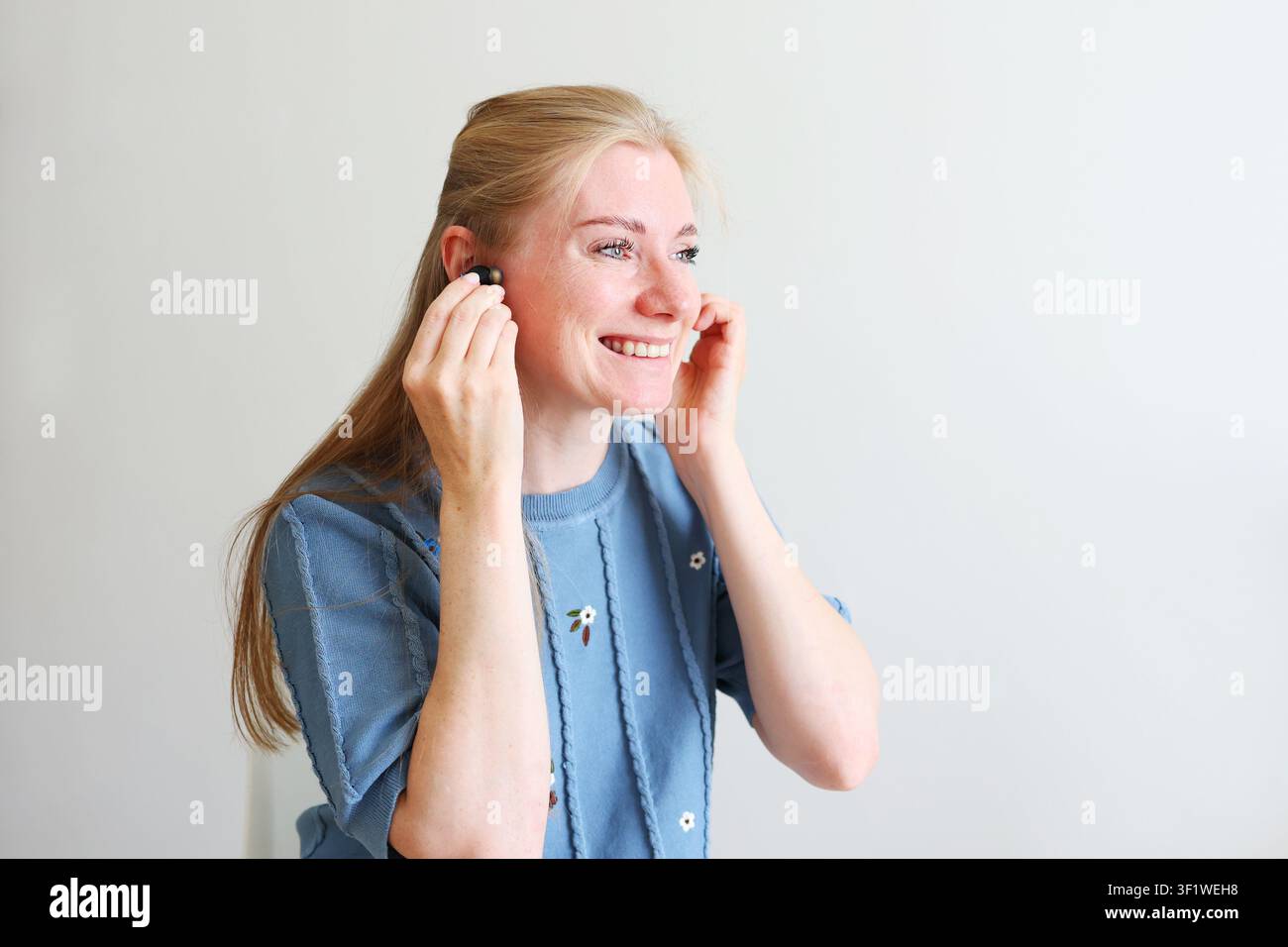 Jeune femme heureuse préparant des écouteurs sans fil pour le travail, les études, la forme physique ou les divertissements dans un cadre intérieur lumineux. Banque D'Images
