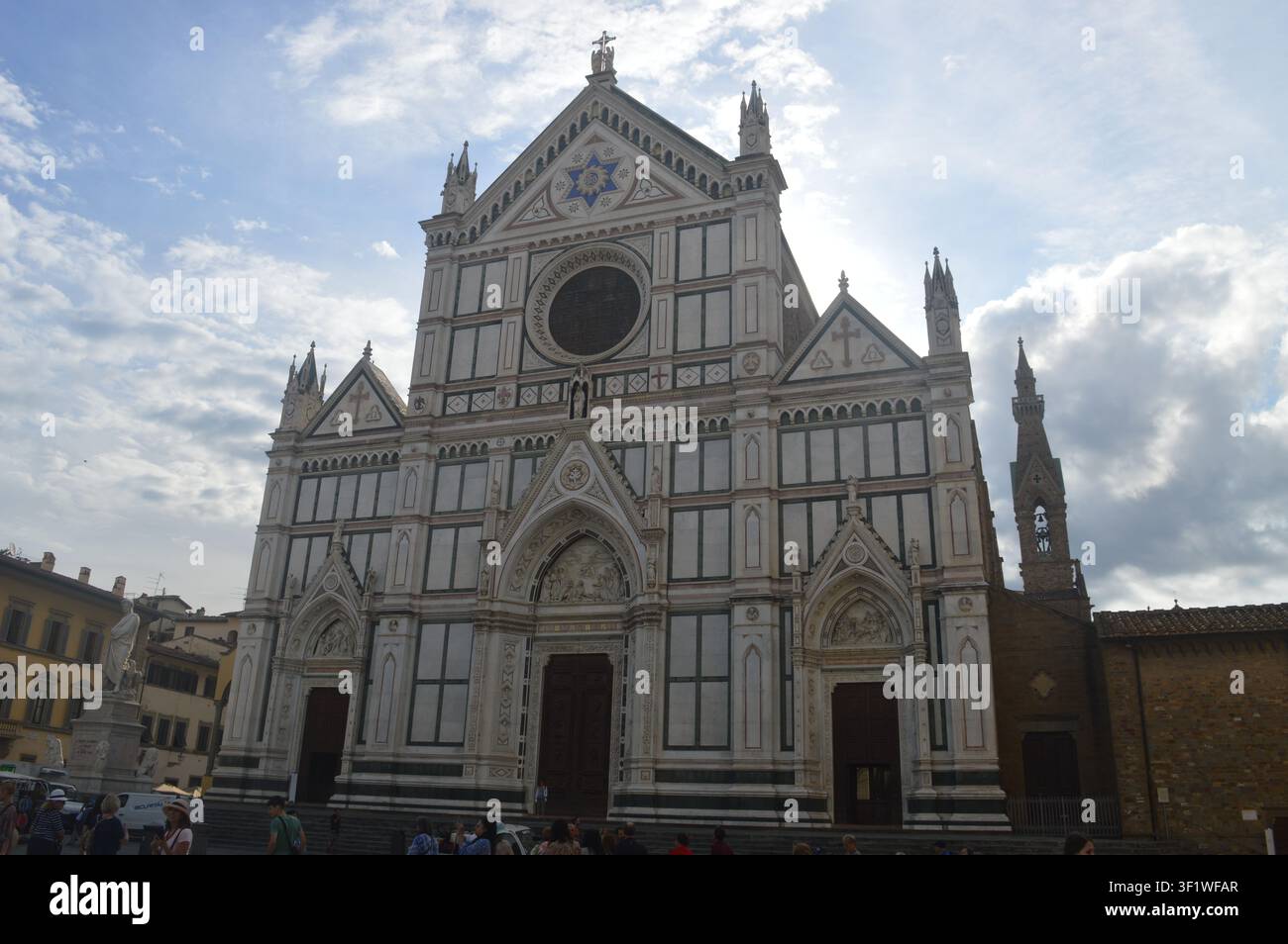 La belle façade en marbre polychrome de la Basilique Santa Croce à Florence, Italie, vue depuis la piazza animée sous un ciel nuageux. Banque D'Images