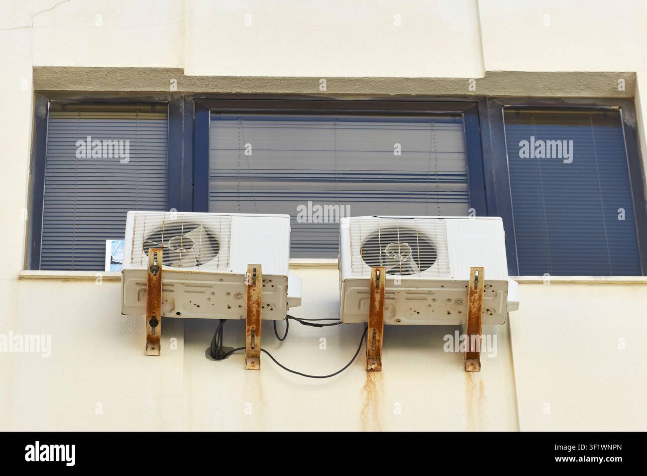 Deux unités extérieures de climatisation anciennes avec supports métalliques rouillés fixés à un mur de bâtiment sous une fenêtre. Banque D'Images