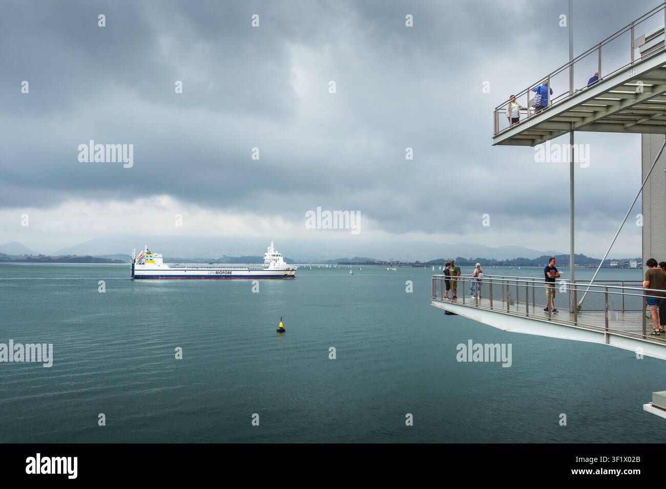 Santander, Espagne - 1er août 2024 : Points de vue depuis les balcons du Centre Botín avec des touristes, la baie de Santander et un navire de charge en transit Banque D'Images