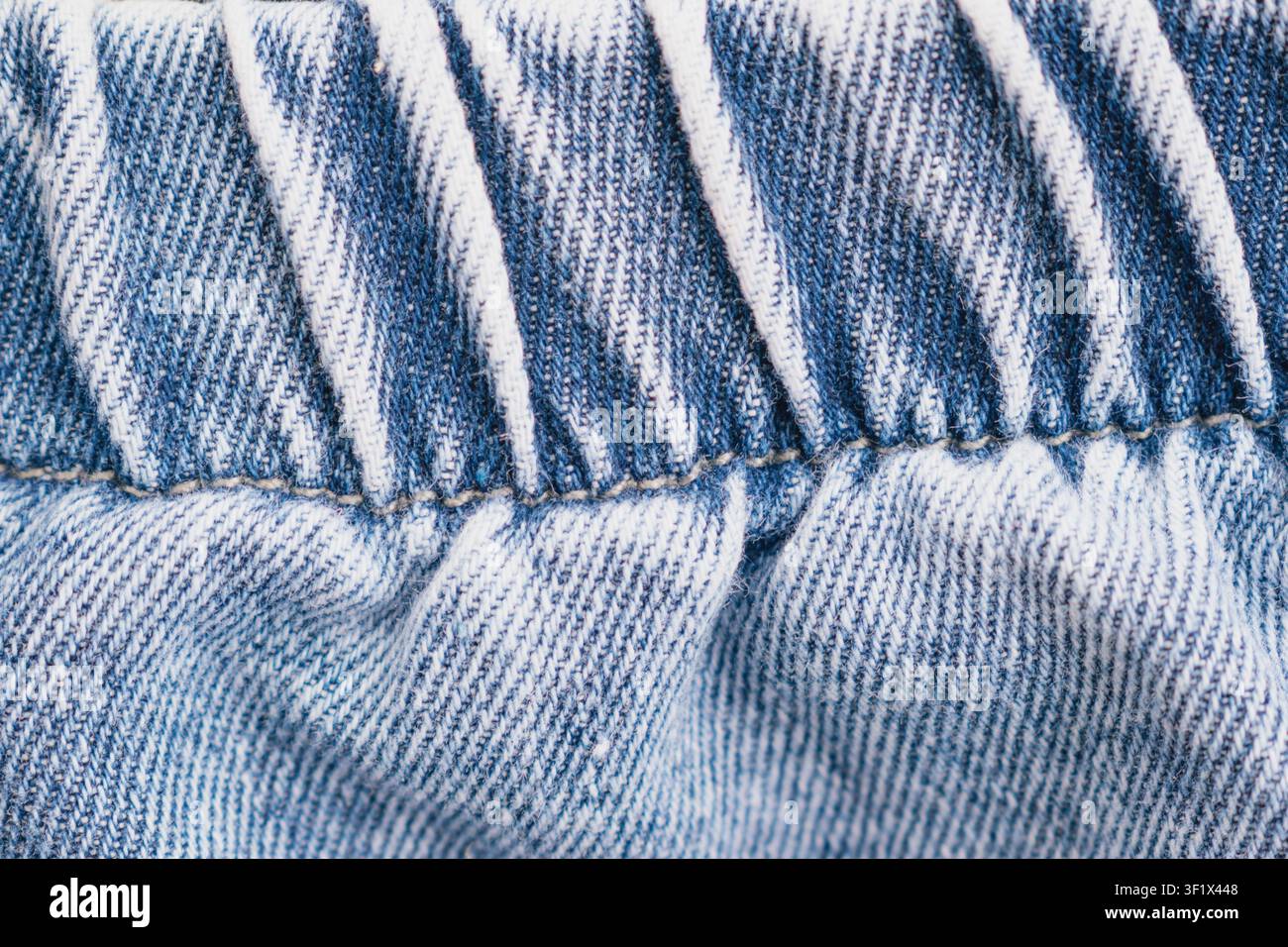 Prise de vue macro horizontale en gros plan d'une ceinture en jean bleu avec bande élastique étirant et détails de points verticaux blancs sur un pantalon décontracté classique Banque D'Images