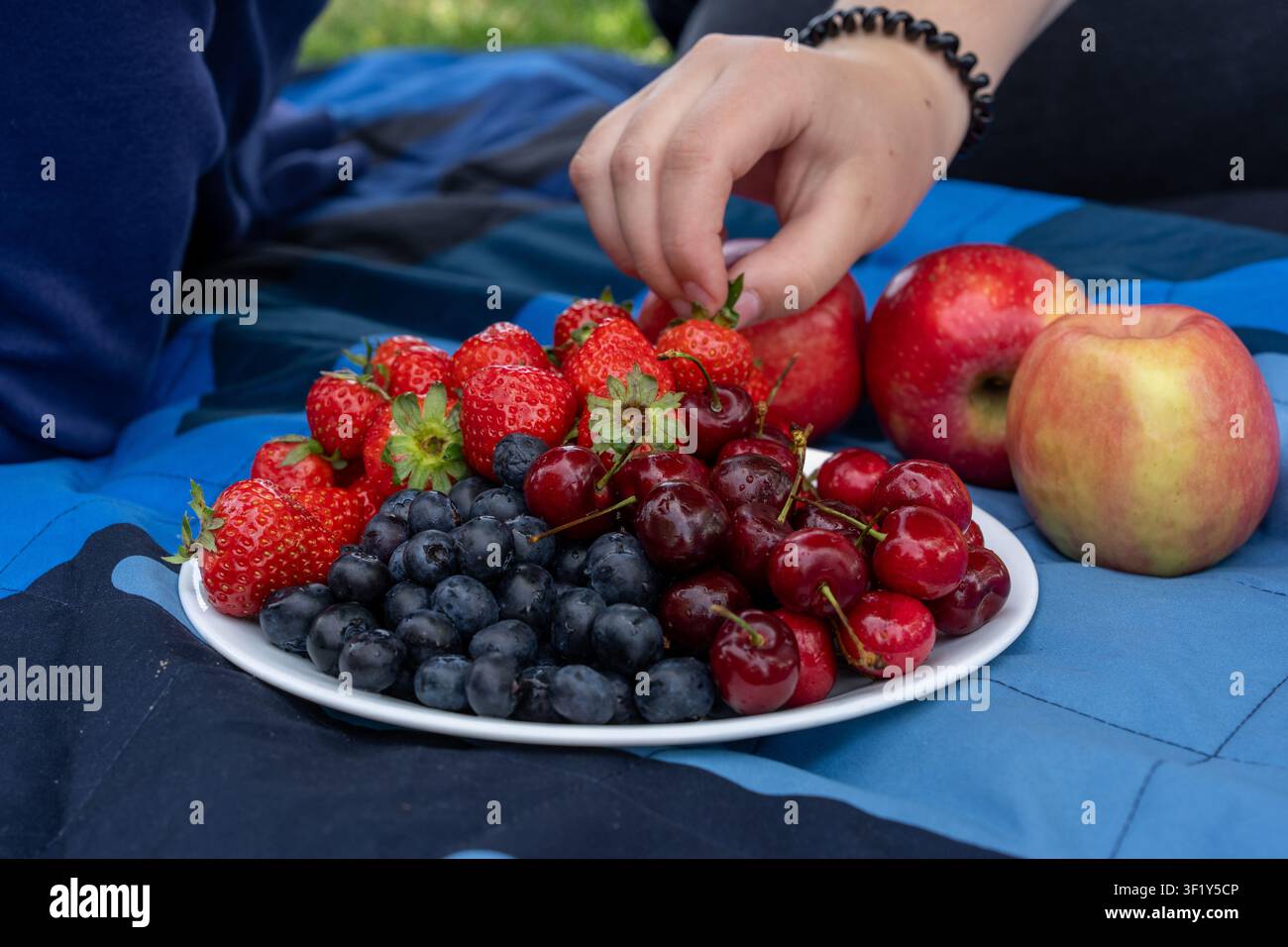 Un plan rapproché horizontal de style vie d'une assiette blanche remplie de fraises fraîches mûres, de myrtilles et de cerises sucrées, à côté de pommes rouges sur un bl Banque D'Images