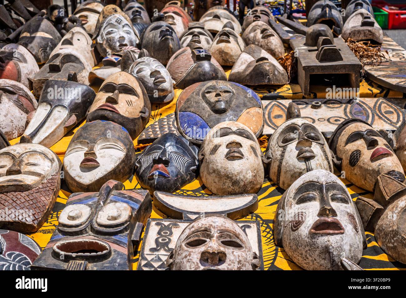 Un cliché d'une grande variété de masques ethniques traditionnels, principalement fabriqués à la main en bois avec des motifs tribaux africains, exposés à la vente sur un fond jaune Banque D'Images