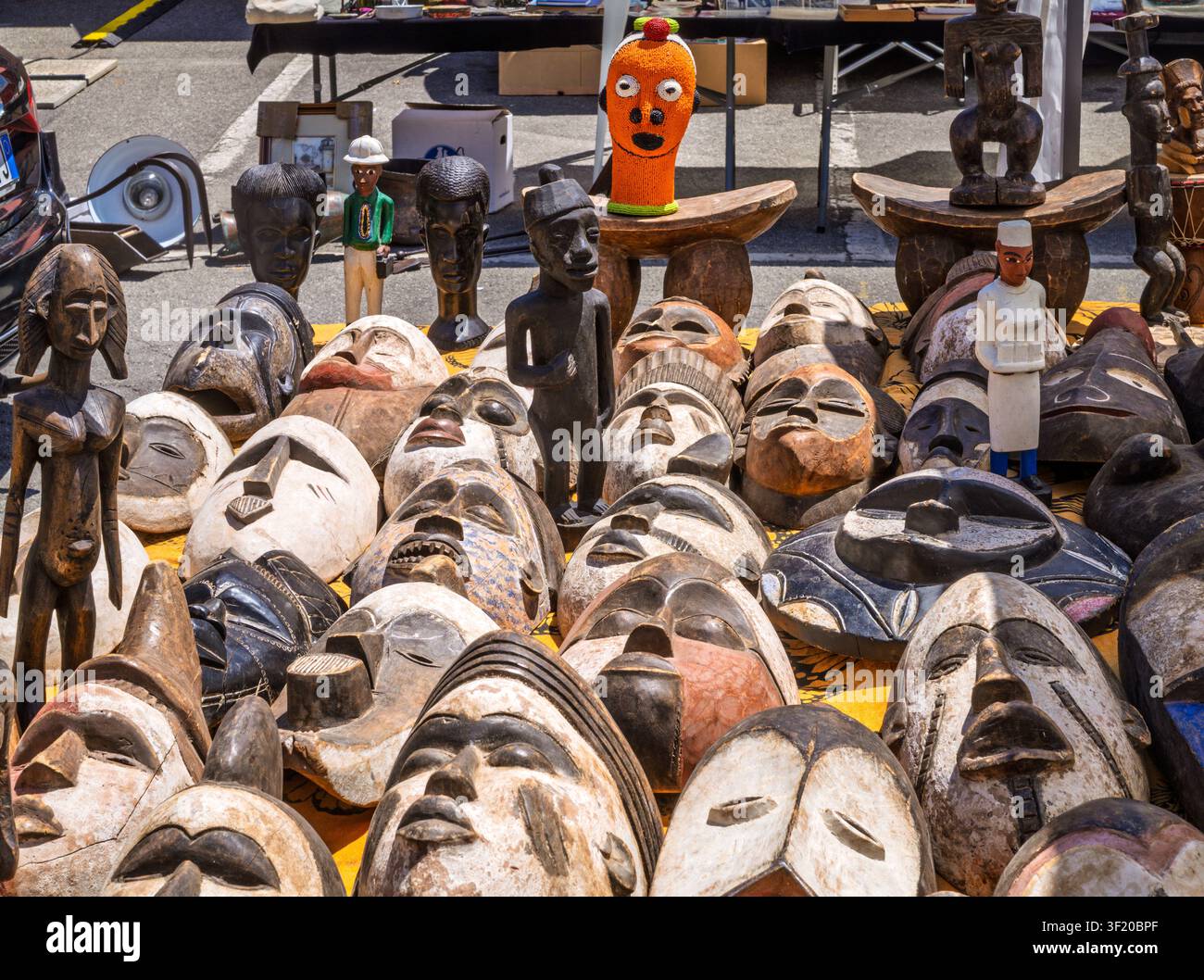 Une photo d'une grande variété de masques et d'idoles ethniques traditionnels, principalement fabriqués à la main en bois avec des motifs tribaux africains, exposés à la vente sur un jaune Banque D'Images