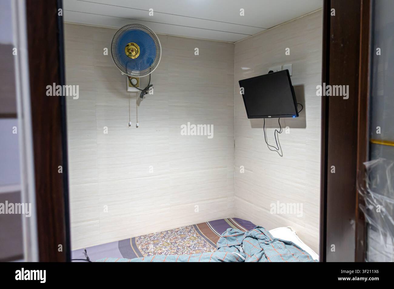 Chambre d'hôtel compacte dans une maison d'hôtes de Hong Kong, dans les Chungking Mansions, avec des murs carrelés, un petit lit et une télévision murale. Banque D'Images
