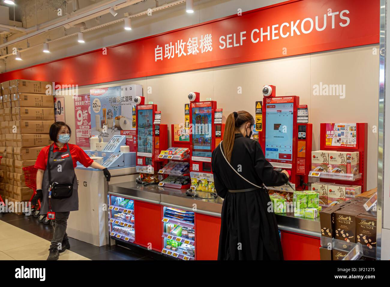 Un client et un membre du personnel dans la zone de caisse automatique d'un supermarché Wellcome à Hong Kong Banque D'Images
