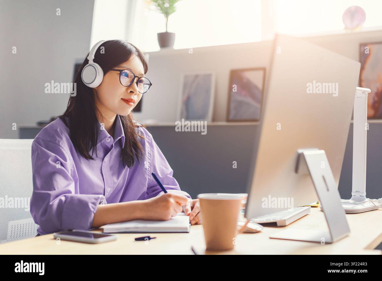 Femme asiatique concentrée portant des écouteurs et travaillant à son bureau à domicile, concept commercial Banque D'Images