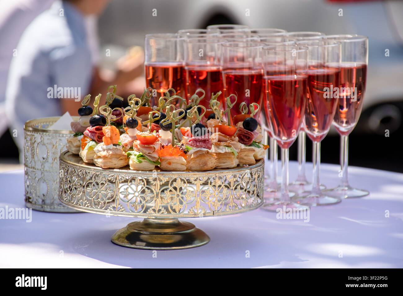 Installation élégante de catering en plein air sur une nappe blanche, avec des boissons pré-remplies et des hors-d'œuvre prêts pour une célébration Banque D'Images