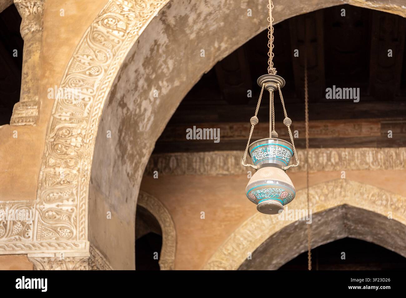 Le Caire, Égypte, 26.07.21. Lampe arabe turquoise suspendue avec inscriptions et arcs pointus ornés de décorations en stuc sculpté, mosquée d’Ibn Tulun. Banque D'Images