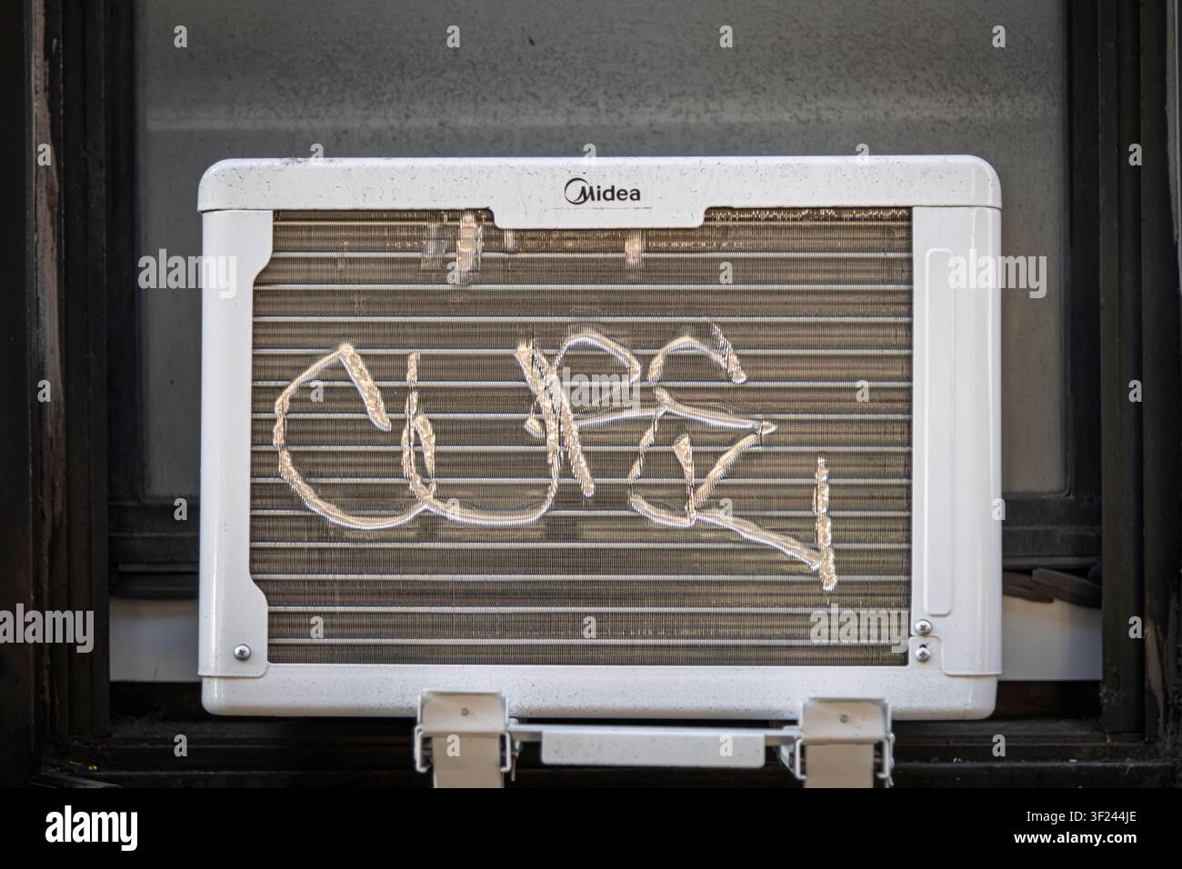 Une signature de graffiti gribouillée sur les lamelles d'une unité de climatisation de fenêtre. Banque D'Images