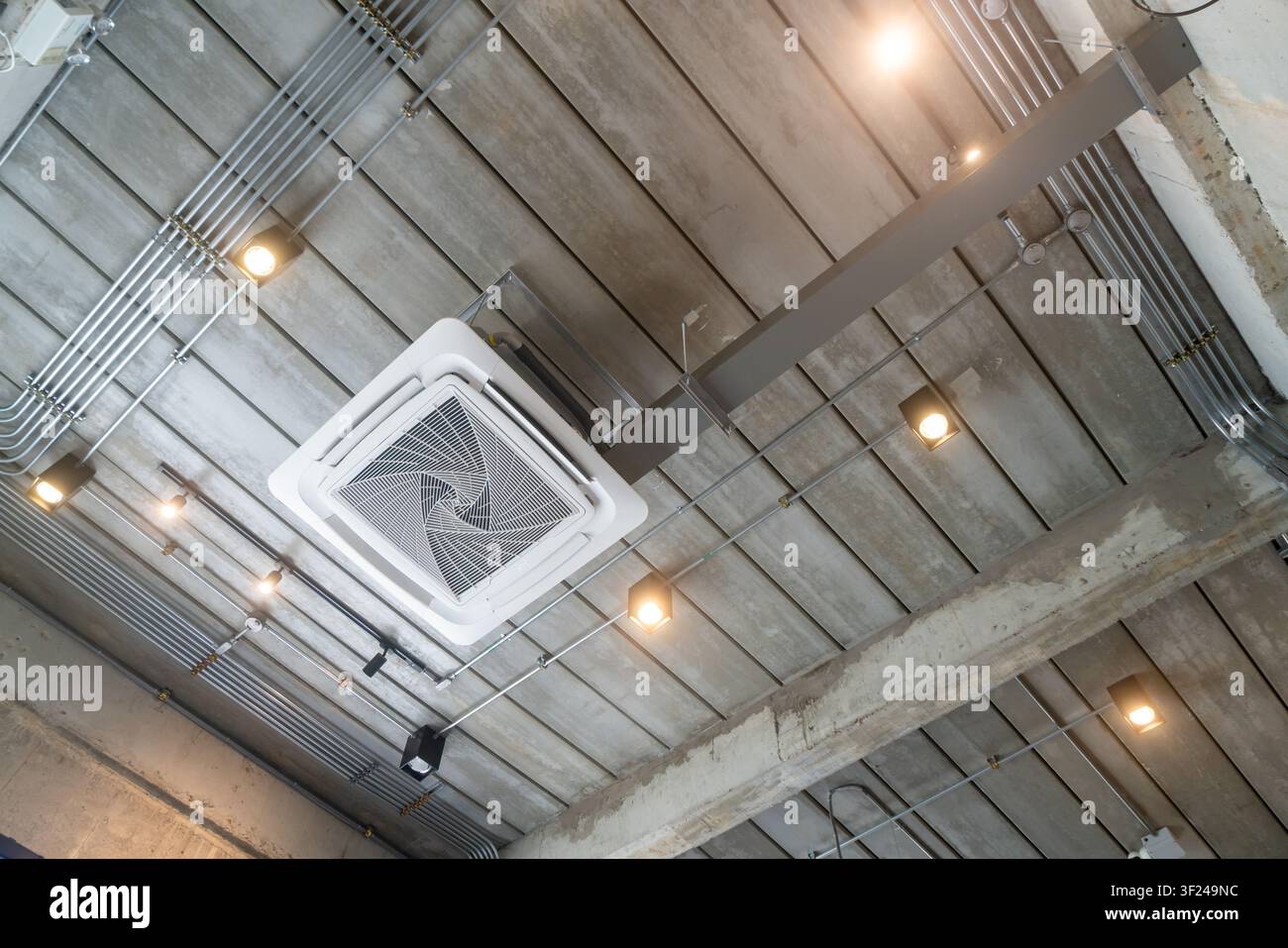 L'image met en valeur un plafond intérieur industriel moderne présentant du béton apparent, des tuyaux métalliques et des conduits, complétés par un éclairage installé et Banque D'Images