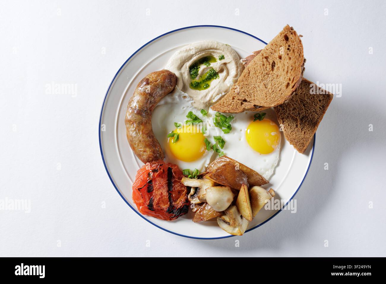 Une assiette de petit-déjeuner vibrante mettant en vedette des œufs frits, de la saucisse, des tomates grillées, des champignons et du pain, parfaite pour les blogs culinaires ou les menus de restaurant. Banque D'Images