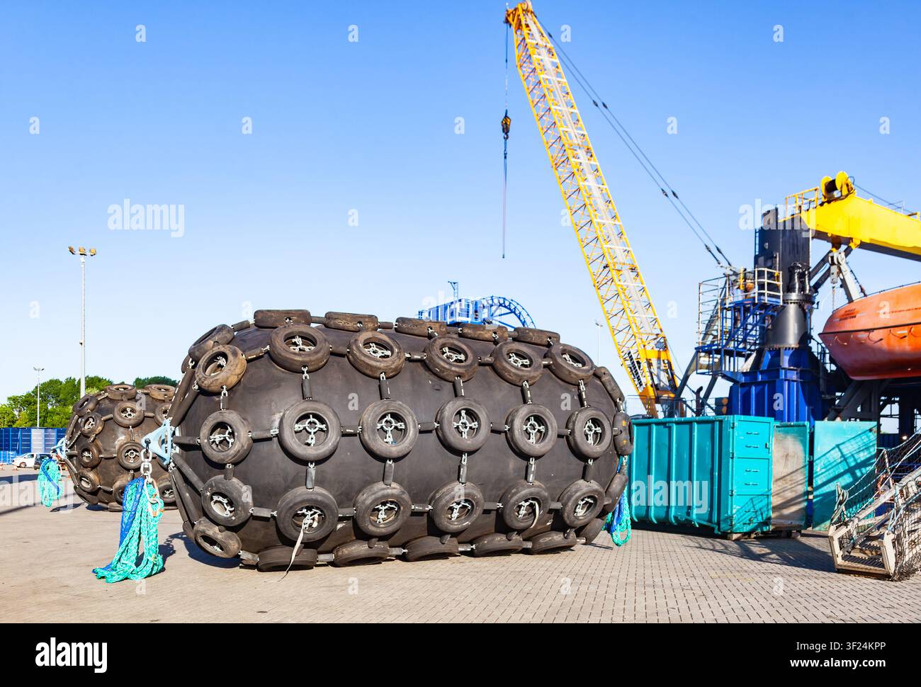 Grands pare-battage pneumatiques en caoutchouc avec filets de pneus à chaînes stockés dans un terminal portuaire maritime près d'une grue sur chenilles industrielle Banque D'Images