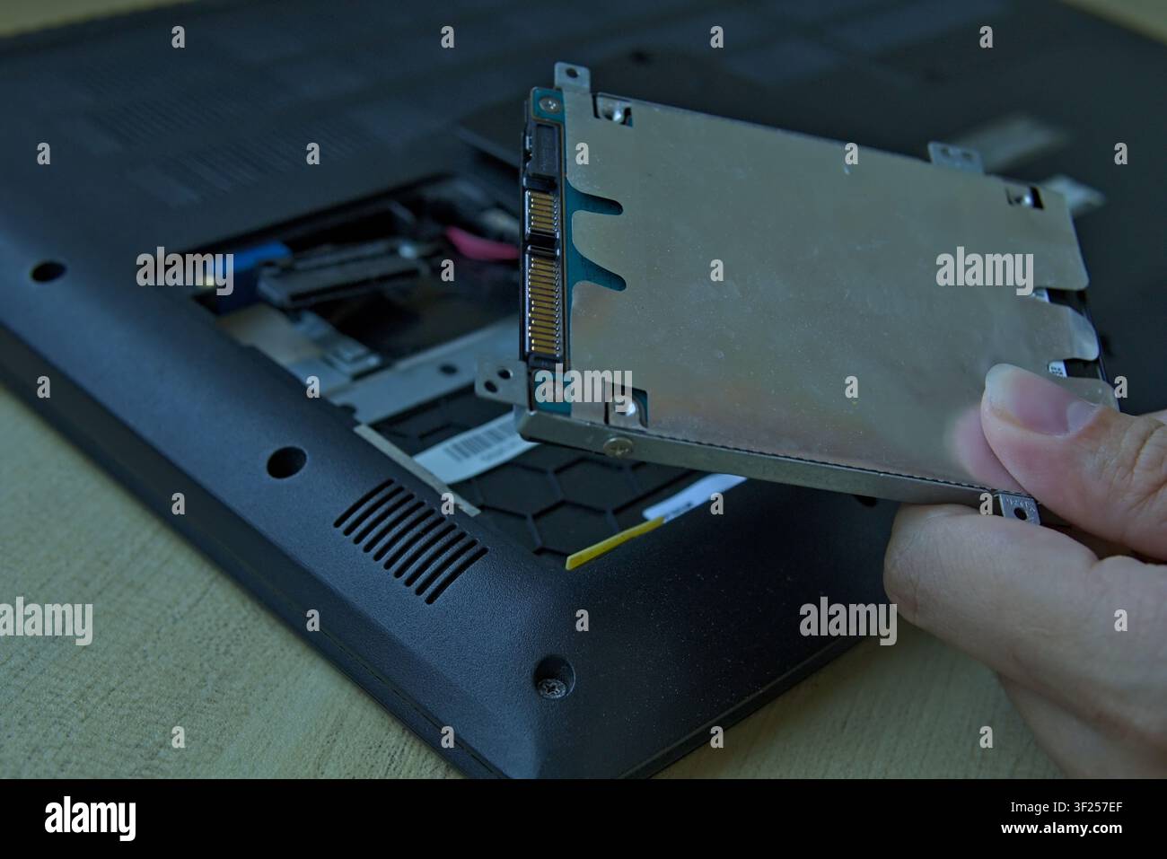Gros plan d'une main retirant soigneusement un disque dur SATA de 2,5 pouces (HDD) dans son support métallique d'une baie d'ordinateur portable ouverte. Banque D'Images