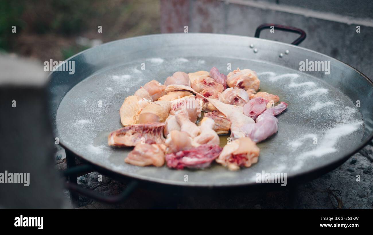Cuire de la paella avec des morceaux de poulet cru dans une grande poêle Banque D'Images