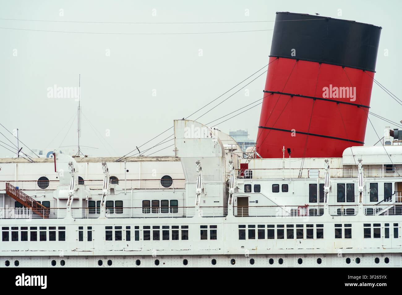 Long Beach, CA, États-Unis - 5 juin 2026 : Fenêtres et hublots avec le fumoir rouge sur le Queen Mary amarré à Long Beach, Californie, par une journée nuageuse. Banque D'Images