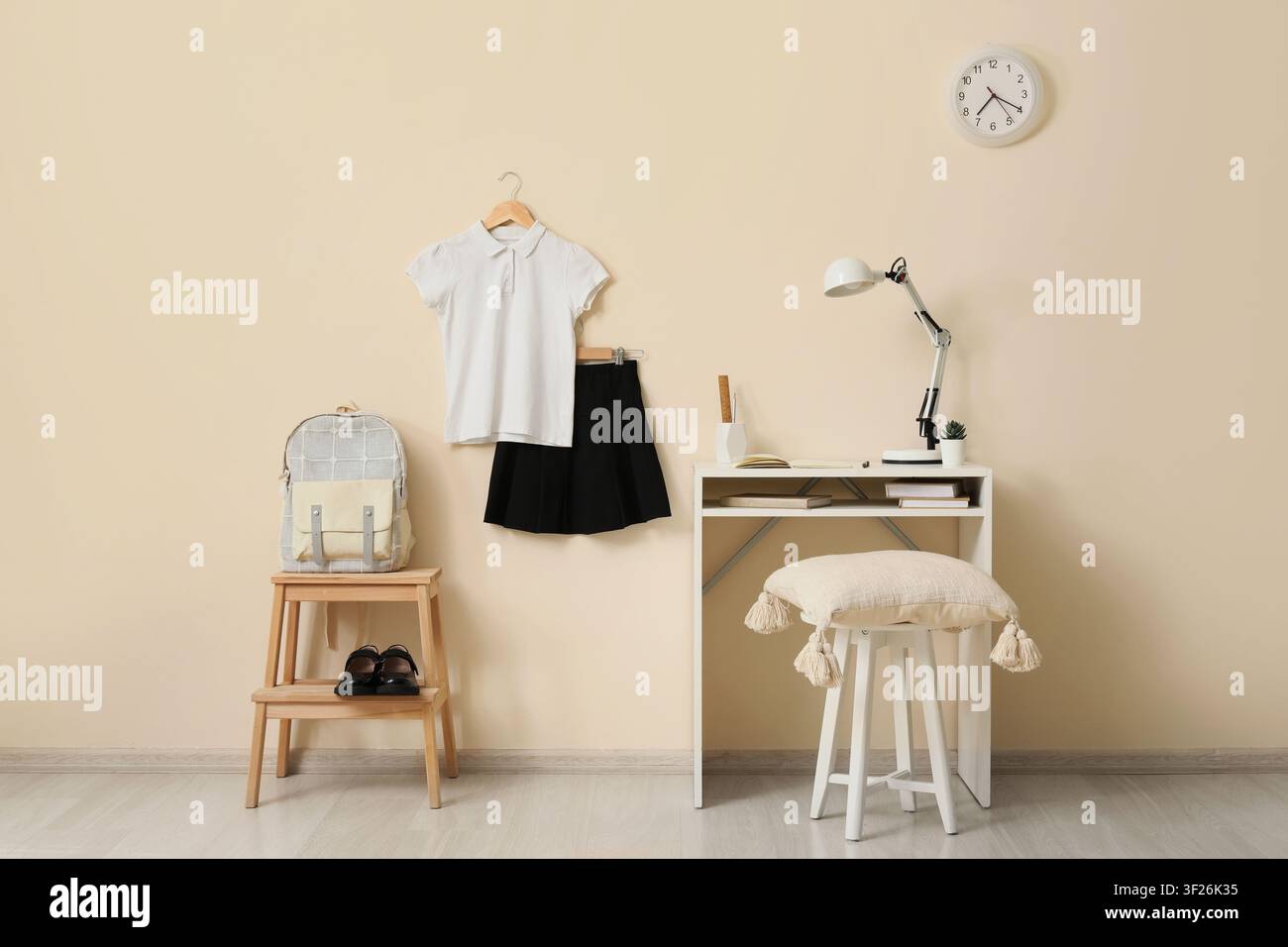 Uniforme scolaire avec sac à dos et chaussures Mary Jane à côté d'un bureau d'étude avec lampe et horloge sur un mur beige, uniforme scolaire composé d'un polo blanc s Banque D'Images