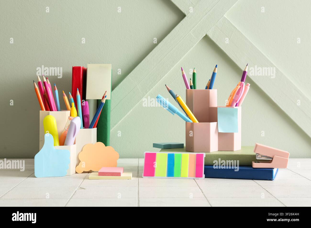 Fournitures scolaires et de bureau colorées avec des crayons, des stylos et des notes adhésives sur un fond vert clair Banque D'Images