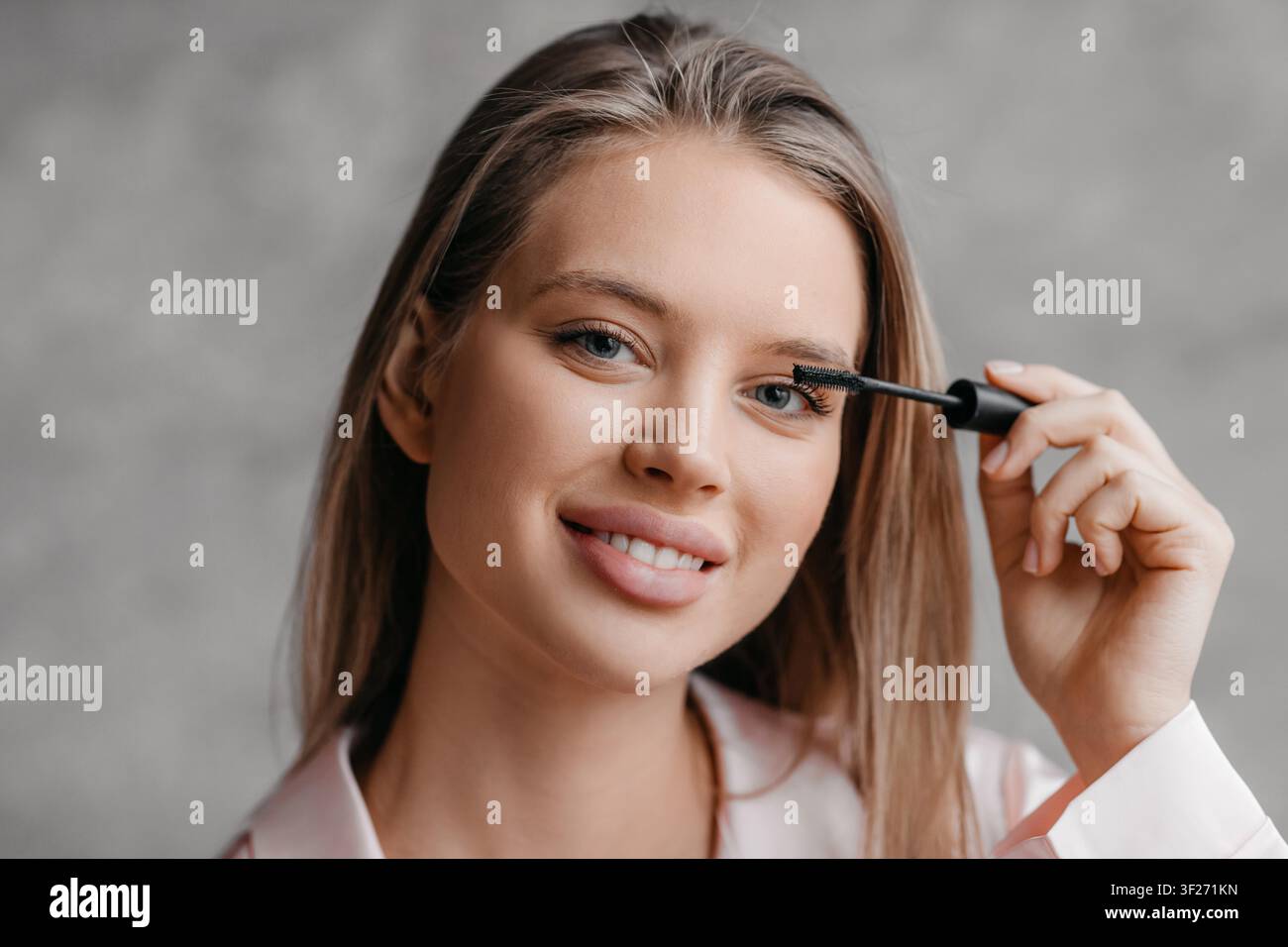 Jeune femme souriante appliquant du mascara tout en regardant la caméra, concept de beauté Banque D'Images