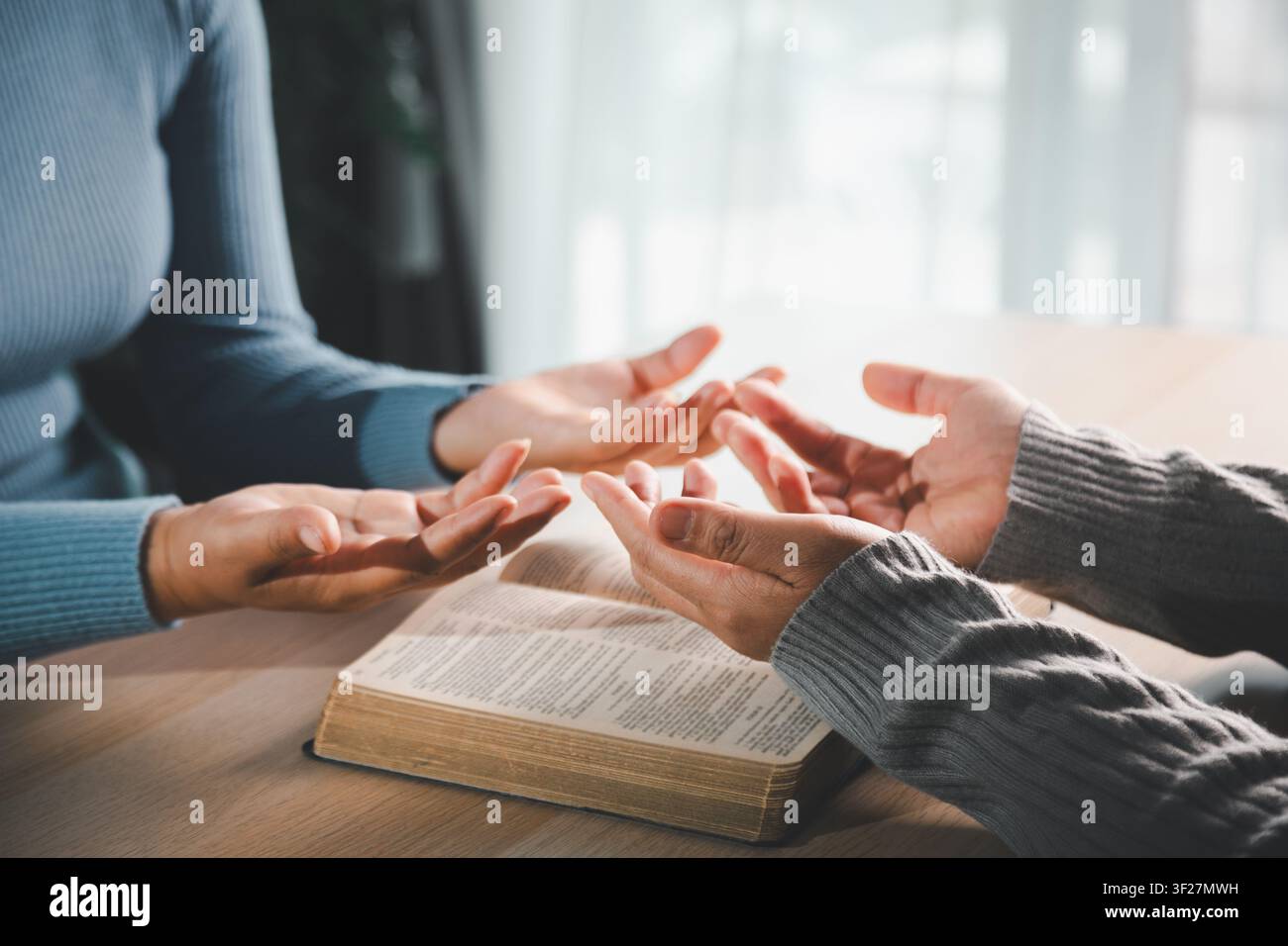 Mains ouvertes priant sur la Bible sur une table en bois avec une lumière douce et chaude, représentant la foi chrétienne, l'adoration, la dévotion, la gratitude, l'espoir et la paix spirituelle Banque D'Images