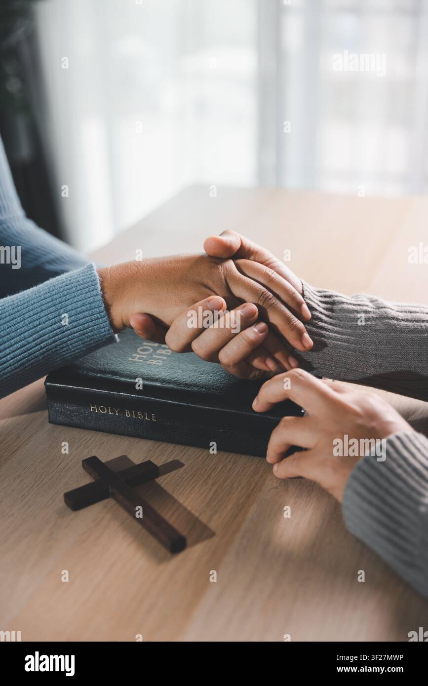 Close up de mains bienveillantes sur une Bible avec une croix en bois sur la table, prière chrétienne, compassion, soins spirituels, espoir, réconfort et guérison Banque D'Images