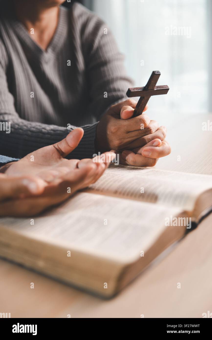 Personne tenant une croix en bois au-dessus d'une Bible ouverte avec une autre main ouverte en prière, foi chrétienne, bénédiction, adoration, soumission et concept d'espoir. Banque D'Images