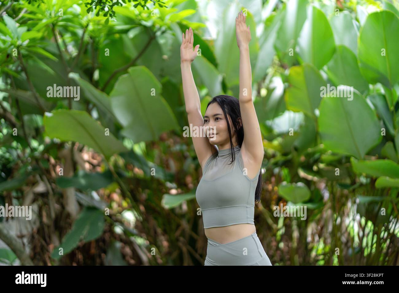 Une Indonésienne réalise une pose de yoga d'équilibre sur un tapis dans un jardin luxuriant en extérieur, mettant en valeur le calme, l'exercice et le bien-être naturel. Banque D'Images