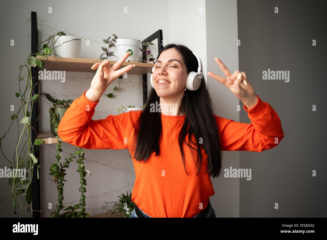 Jeune femme profitant de la musique avec des écouteurs sans fil dans une pièce lumineusement éclairée. Streaming musical, mode de vie positif et divertissement numérique. Banque D'Images