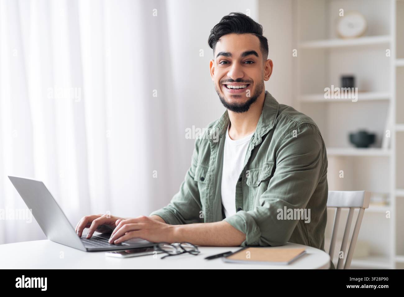 Jeune homme souriant utilisant un ordinateur portable au bureau à domicile, concept commercial Banque D'Images
