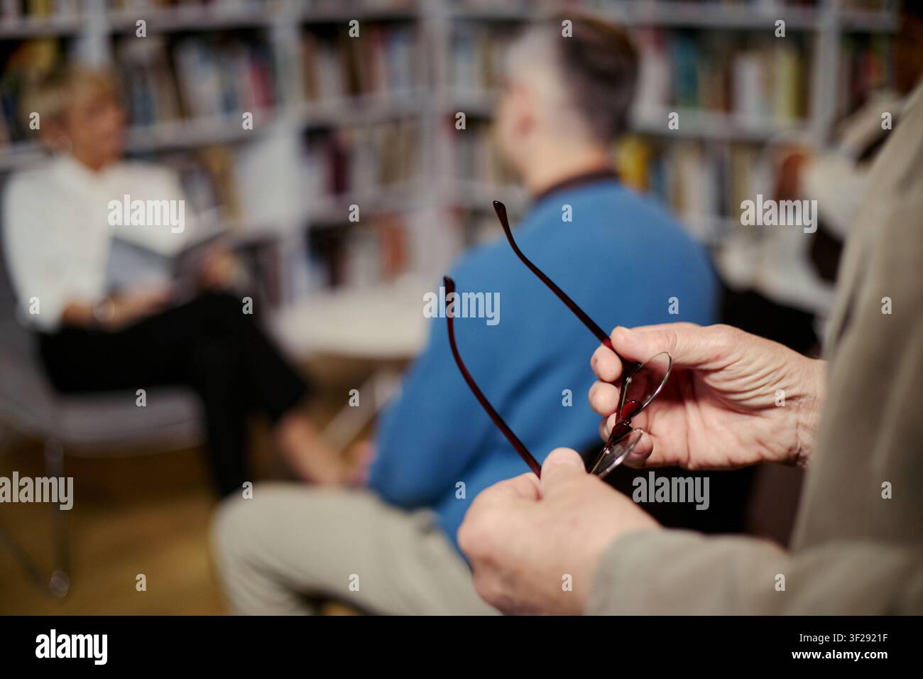 Sénior menant une discussion de groupe dans une bibliothèque, homme d'âge moyen tenant des lunettes tout en écoutant pendant une séance de conseil. Convient pour la santé mentale, les groupes de soutien, le marketing thérapeutique Banque D'Images