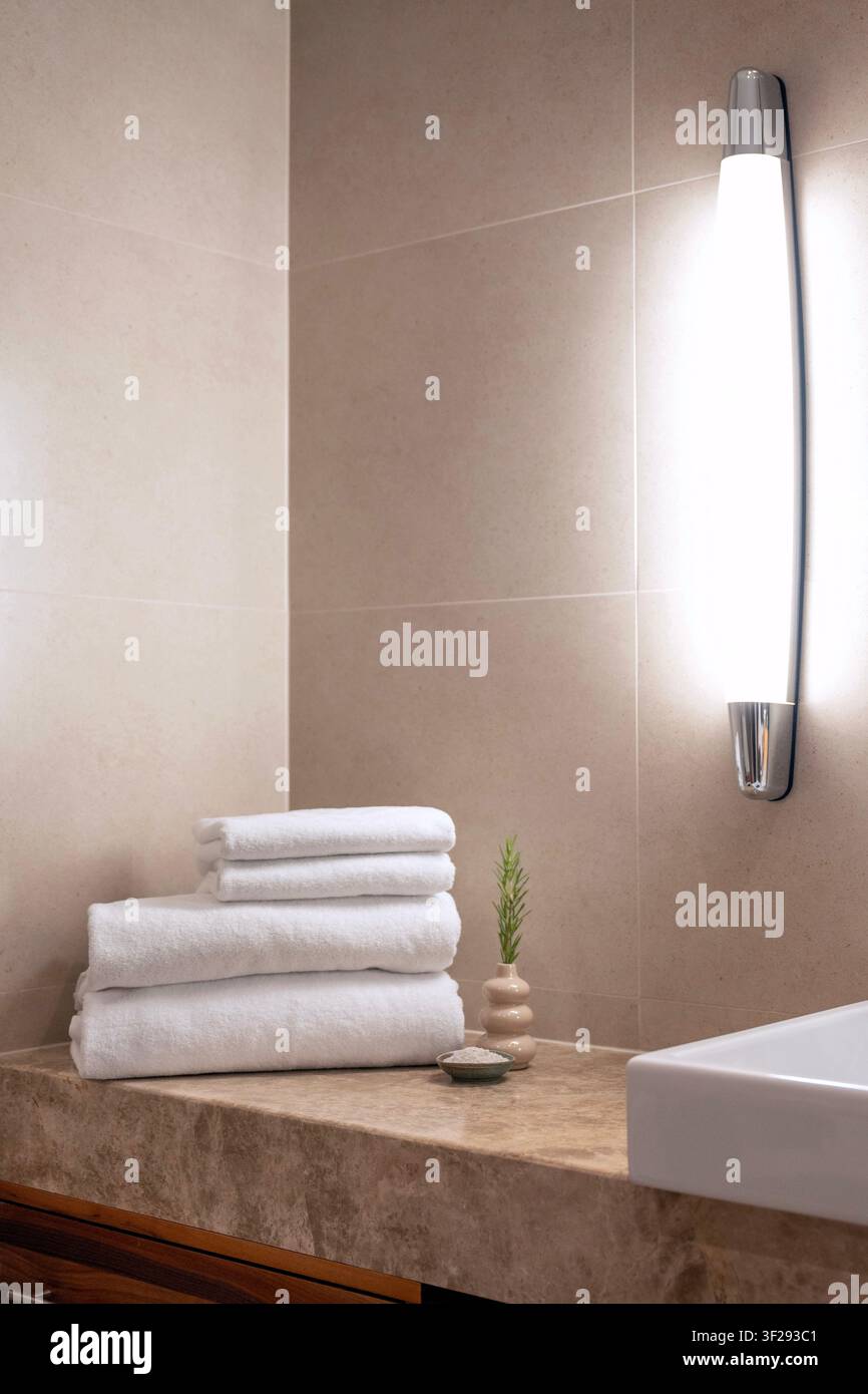 Serviette blanche roulée sur un plateau de bain en bois avec des essentiels de spa dans une salle de bain d'hôtel moderne, créant une atmosphère de bien-être relaxante Banque D'Images