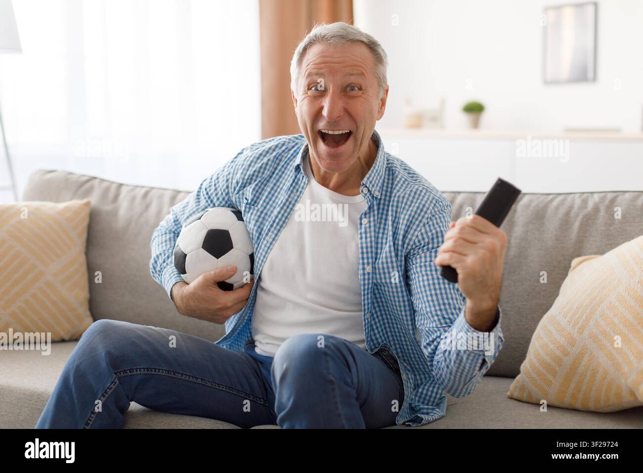 Homme caucasien âgé heureux célébrant un but en regardant le football, salon Banque D'Images