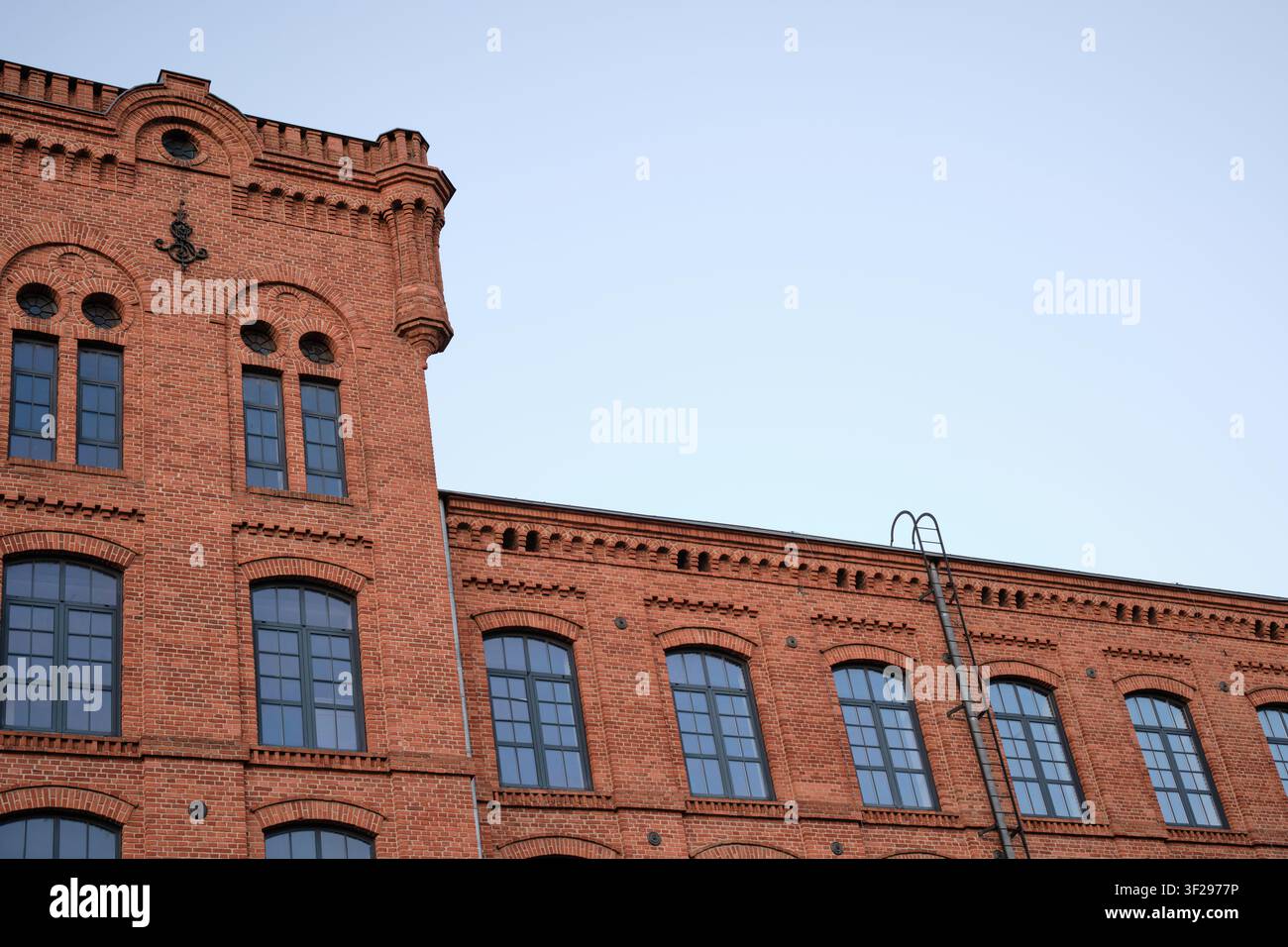 Large façade en briques rouges avec des fenêtres en arc et une échelle sur le toit, combinant l'architecture industrielle et un ciel dégagé pour les mises en page de bannières. Banque D'Images