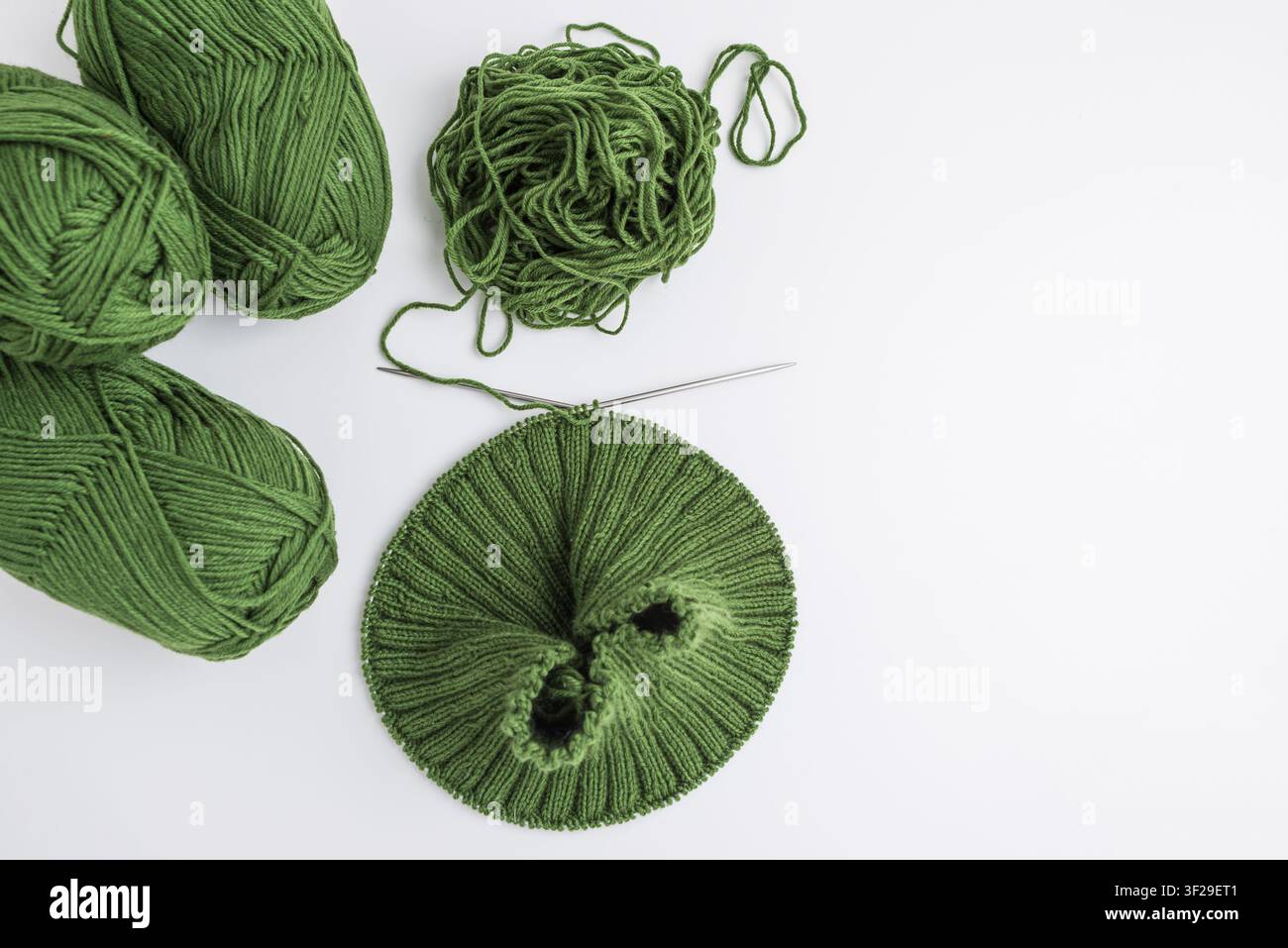 Boules de fil vert, un écheveau emmêlé et un projet de tricot inachevé sur les aiguilles montrant le processus de création de produits textiles faits à la main Banque D'Images