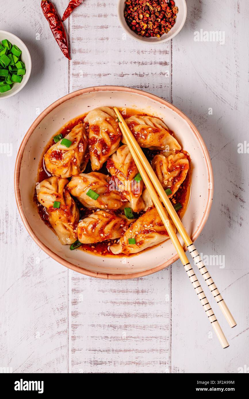 Délicieux boulettes servies dans un bol avec une sauce épicée et des oignons verts sur une table en bois Banque D'Images