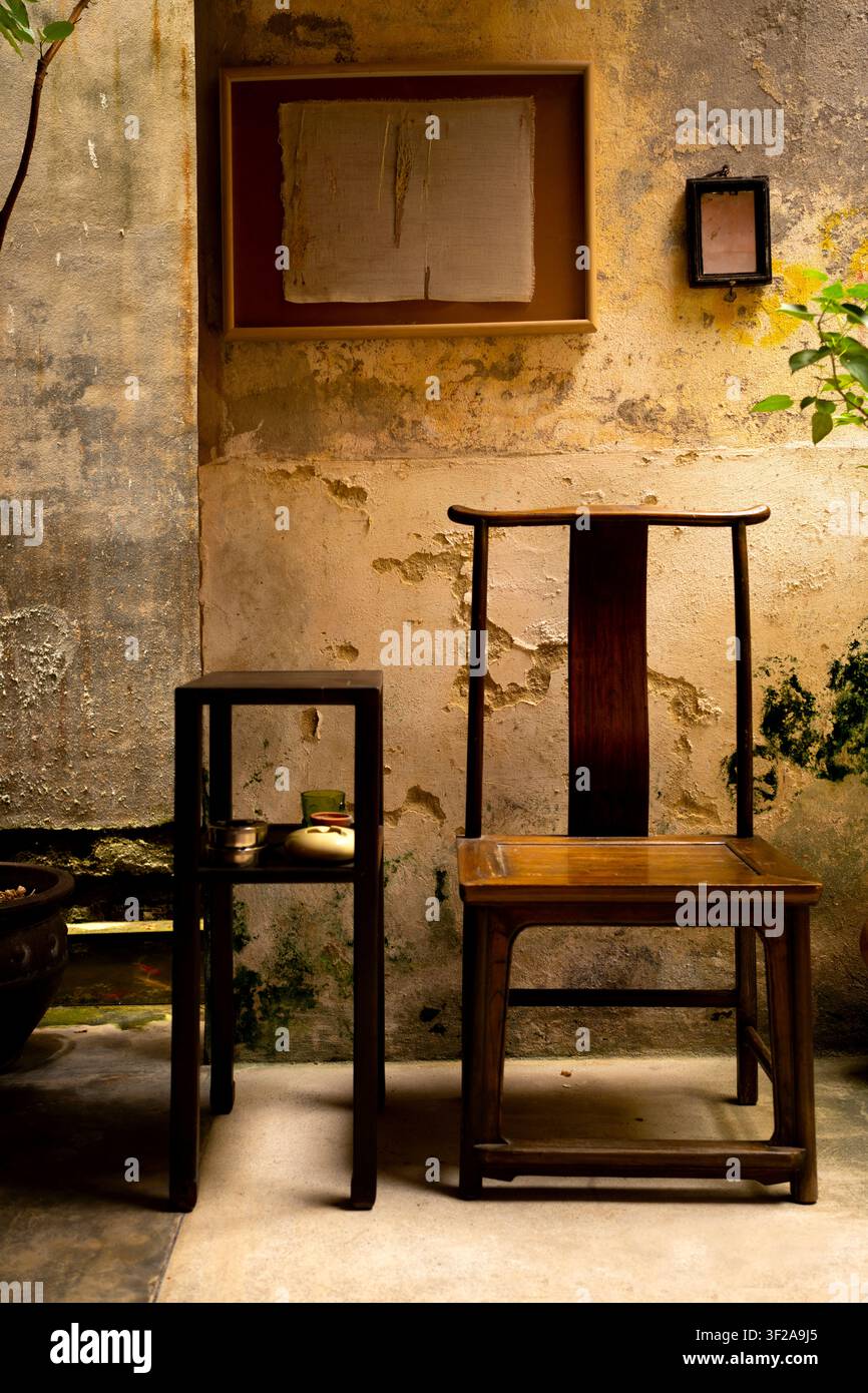 Prise verticale d'une chaise en bois chinoise classique et d'une table d'appoint contre un mur rustique et patiné, décoré d'œuvres d'art encadrées dans une cour Banque D'Images