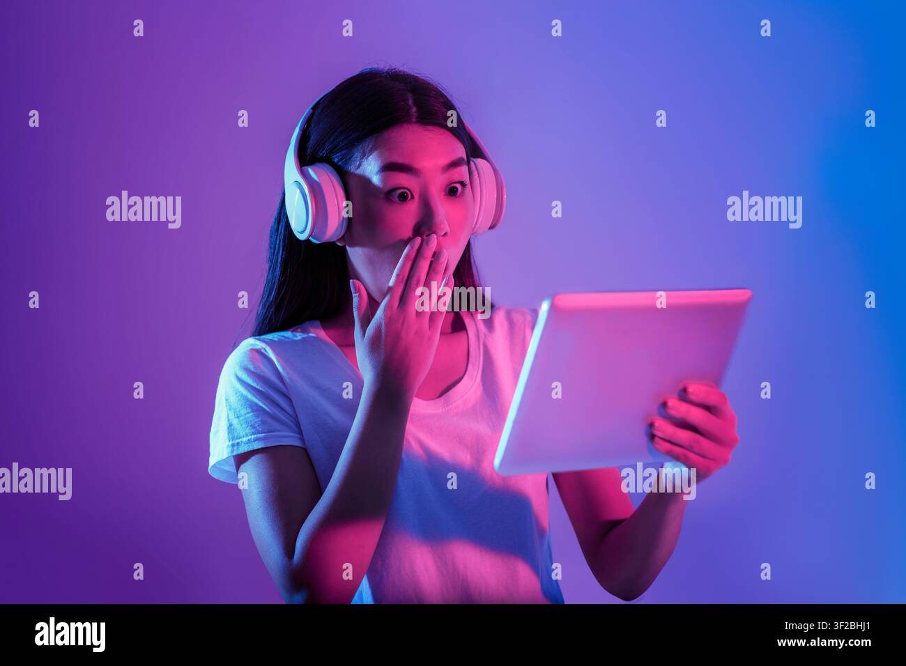 Surprise asiatique fille dans le grand casque ferme la bouche avec la main et regarde la tablette Banque D'Images