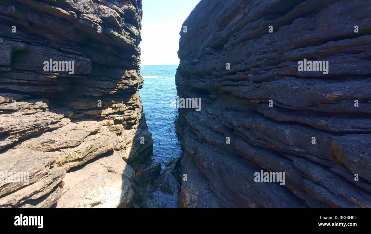 Regardant dans une fissure rocheuse étroite où l'eau claire de l'océan s'écoule entre les parois sombres et stratifiées des falaises à Hook Head Banque D'Images