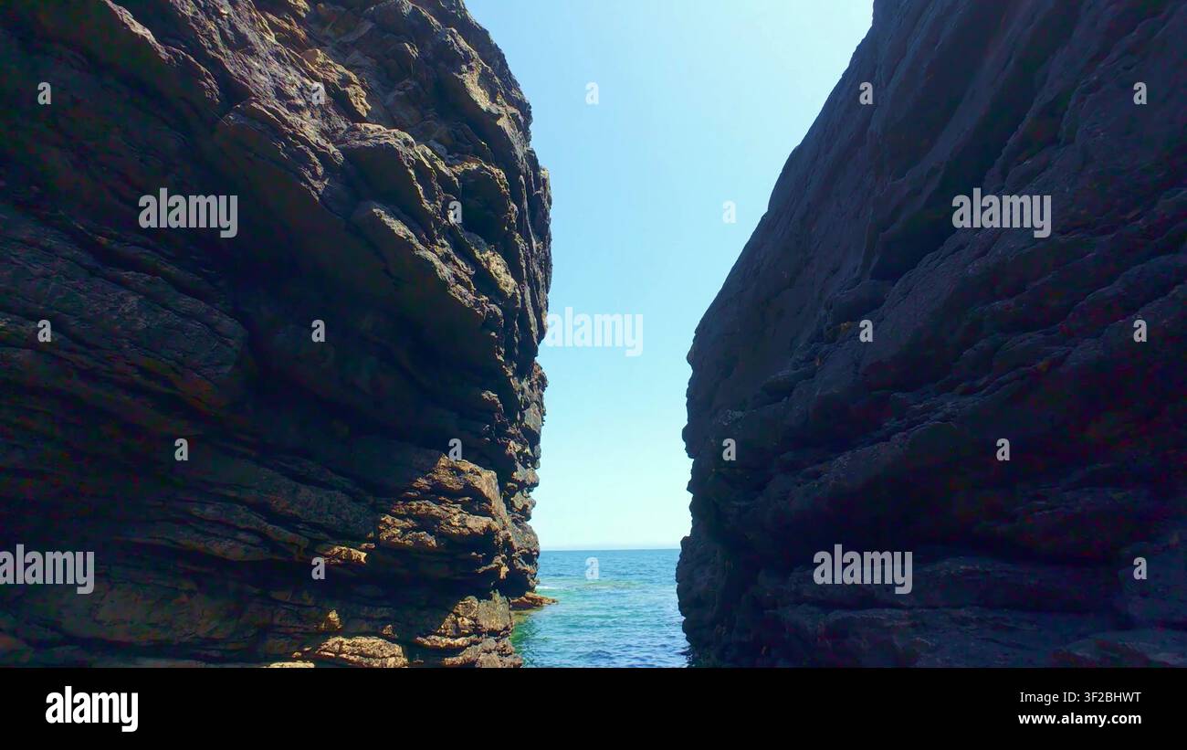 Une vue étroite de l'océan bleu encadrée par des falaises rocheuses sombres, escarpées et stratifiées sous un ciel clair à Hook Head, Irlande. Banque D'Images