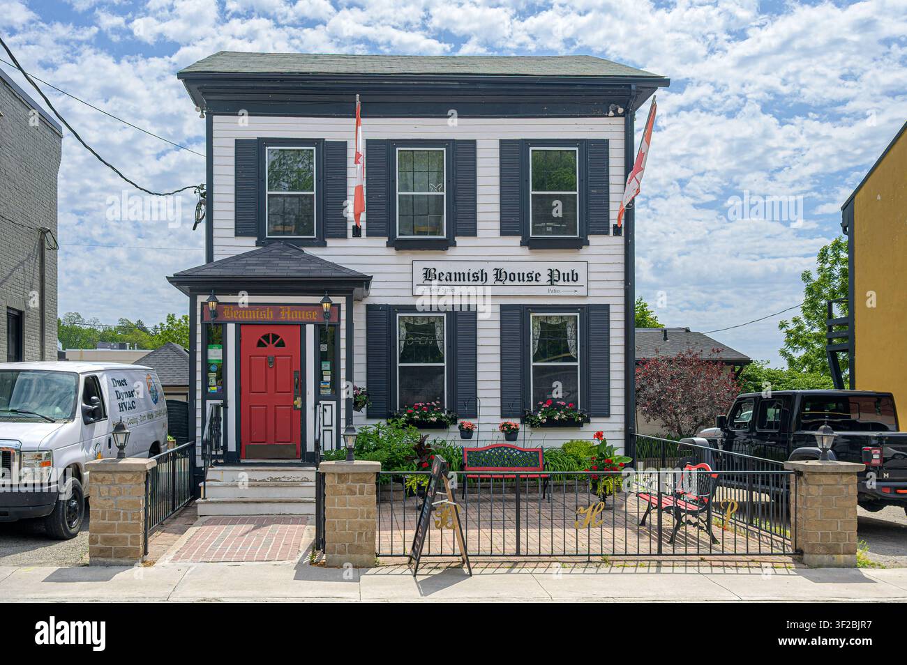 Pub Beamish House avec une terrasse accueillante, une porte d'entrée rouge et des drapeaux canadiens sous un ciel bleu Banque D'Images