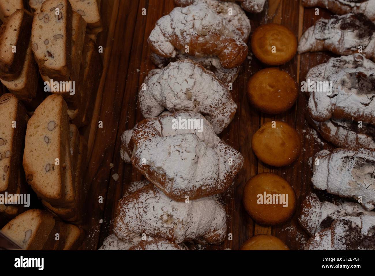 Pâtisseries dorées saupoudrées de sucre glace reposent sur une planche en bois. Les douceurs affichent une chaleur. Idéales pour les menus de café, les blogs culinaires Banque D'Images
