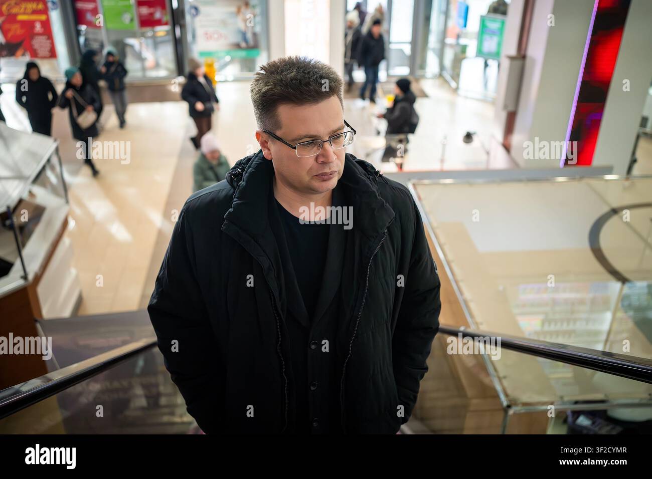 Homme pensif montant un escalier mécanique dans un centre commercial. Ambiance réfléchie et style de vie consumériste urbain. Banque D'Images