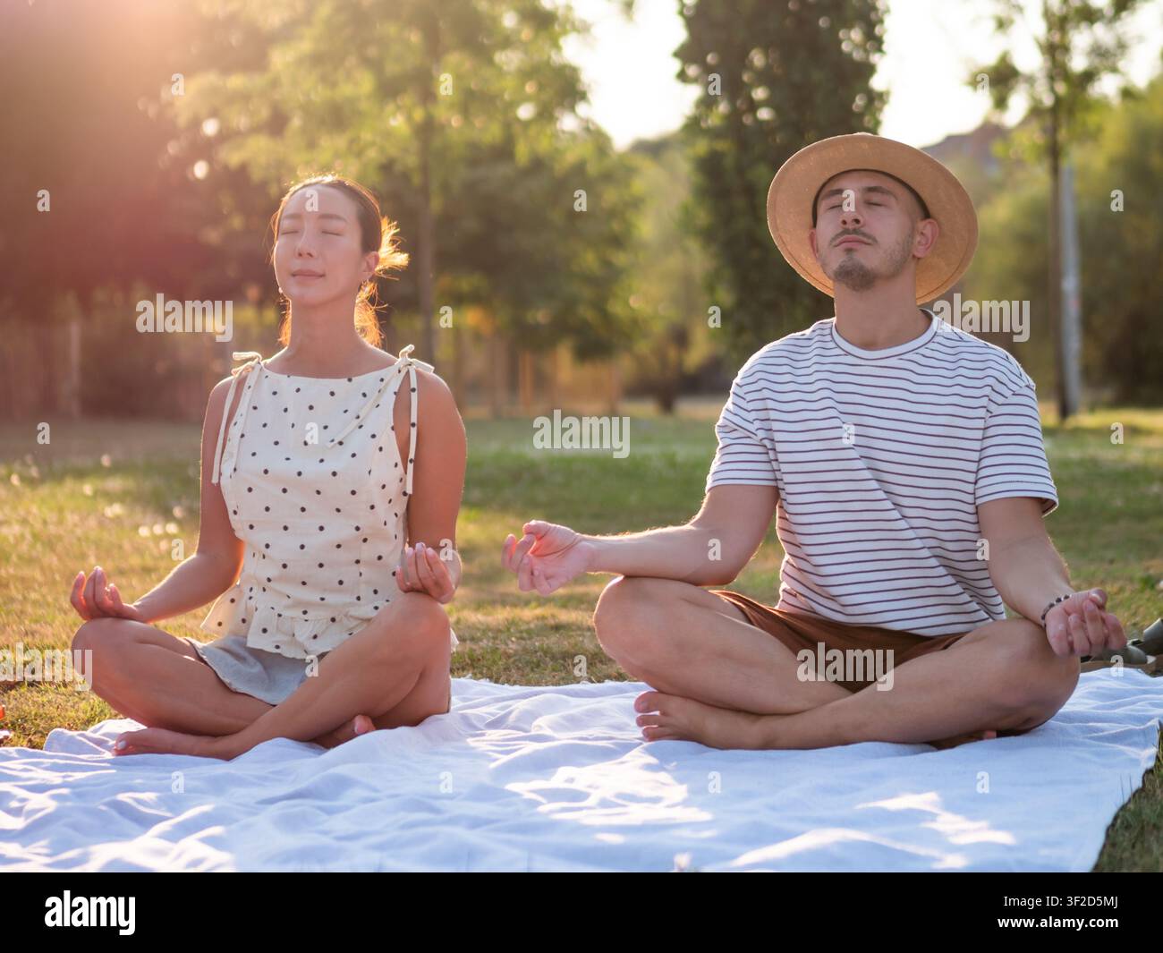 Un couple adulte multiracial pratique le yoga dans un parc en été. Position du lotus. Banque D'Images