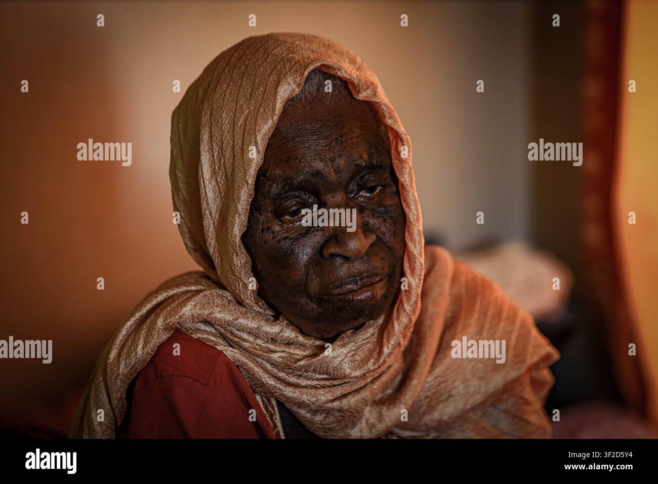 une femme âgée portant un foulard de couleur claire, assise à l'intérieur dans une lumière naturelle douce. Banque D'Images