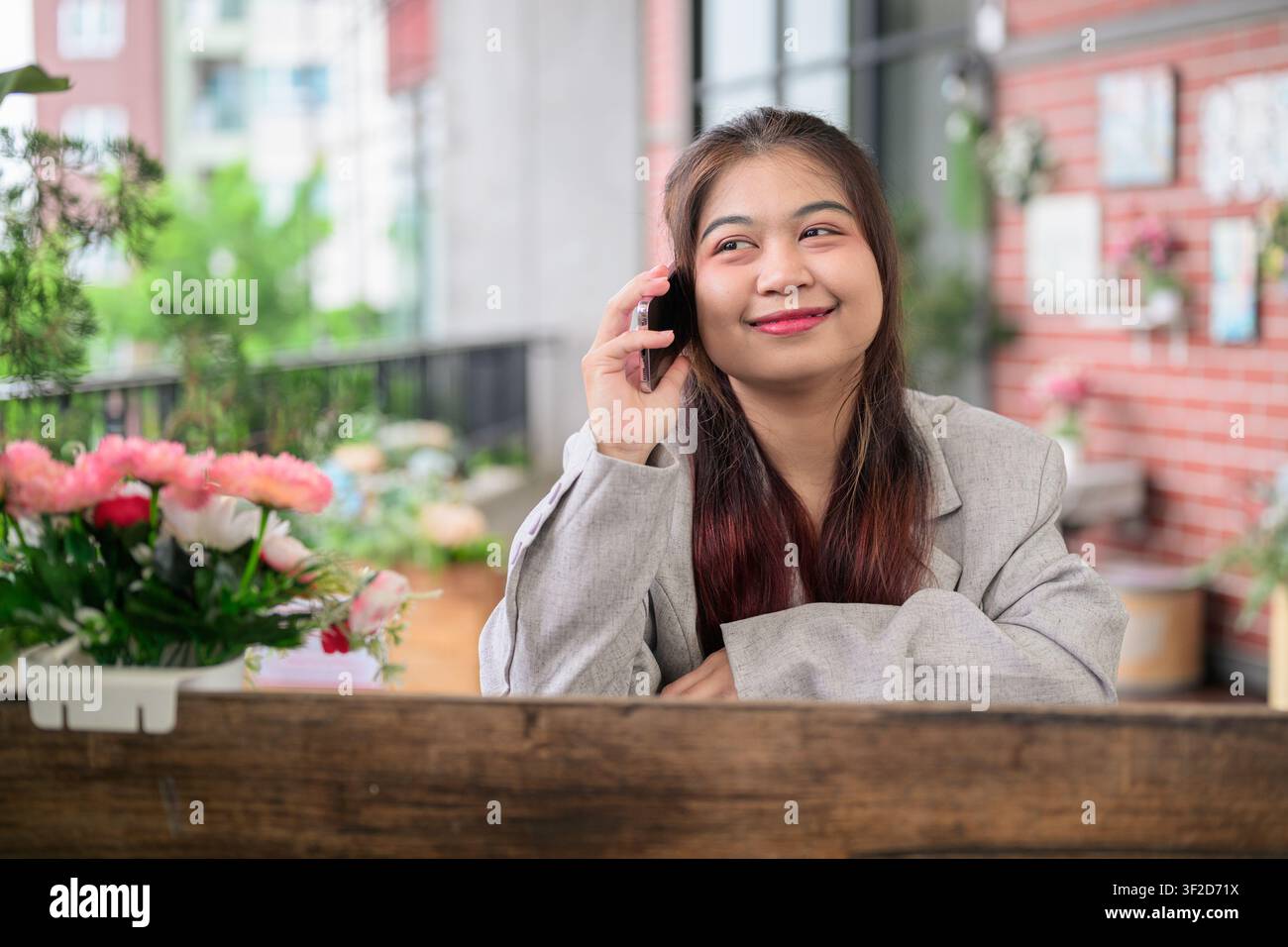 Un plan moyen d'une jeune femme d'affaires thaïe du Sud-Est de l'Isan portant une veste de costume grise, tenant un téléphone portable à son oreille et souriant tout en énumérant Banque D'Images