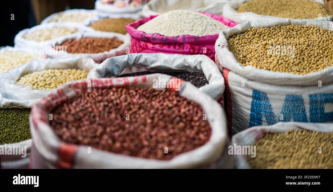 Divers grains bruts, légumes secs et cacahuètes exposés dans des sacs en toile de jute ouverts sur un marché humide traditionnel Banque D'Images