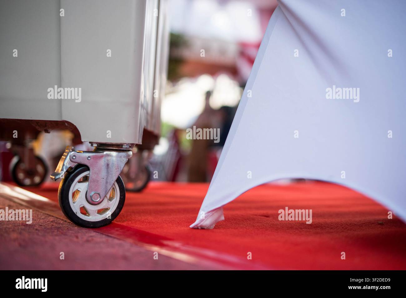 Gros plan de la mise en place de l'événement avec un tapis rouge au sol, un tissu décoratif blanc et une roue d'équipement de catering Banque D'Images
